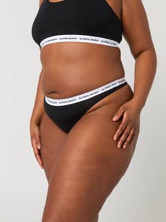 Side view of a model wearing the black Björn Borg Core Logo Thong 2-pack with a white logo elastic waistband. - Image 6