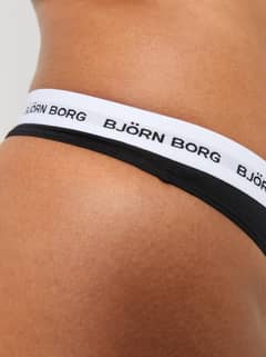 Detailed close-up of the black Core Logo Thong 2-pack, featuring a white logo elastic waistband and soft cotton. - Image 9