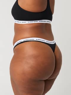 Side view of a woman wearing the black Björn Borg Core Logo Thong 2-pack featuring a white logo elastic waistband. - Image 7