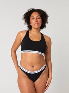 Front view of a model wearing the black Core Logo Thong 2-pack in soft cotton stretch featuring a mid-rise waist. - Image 1