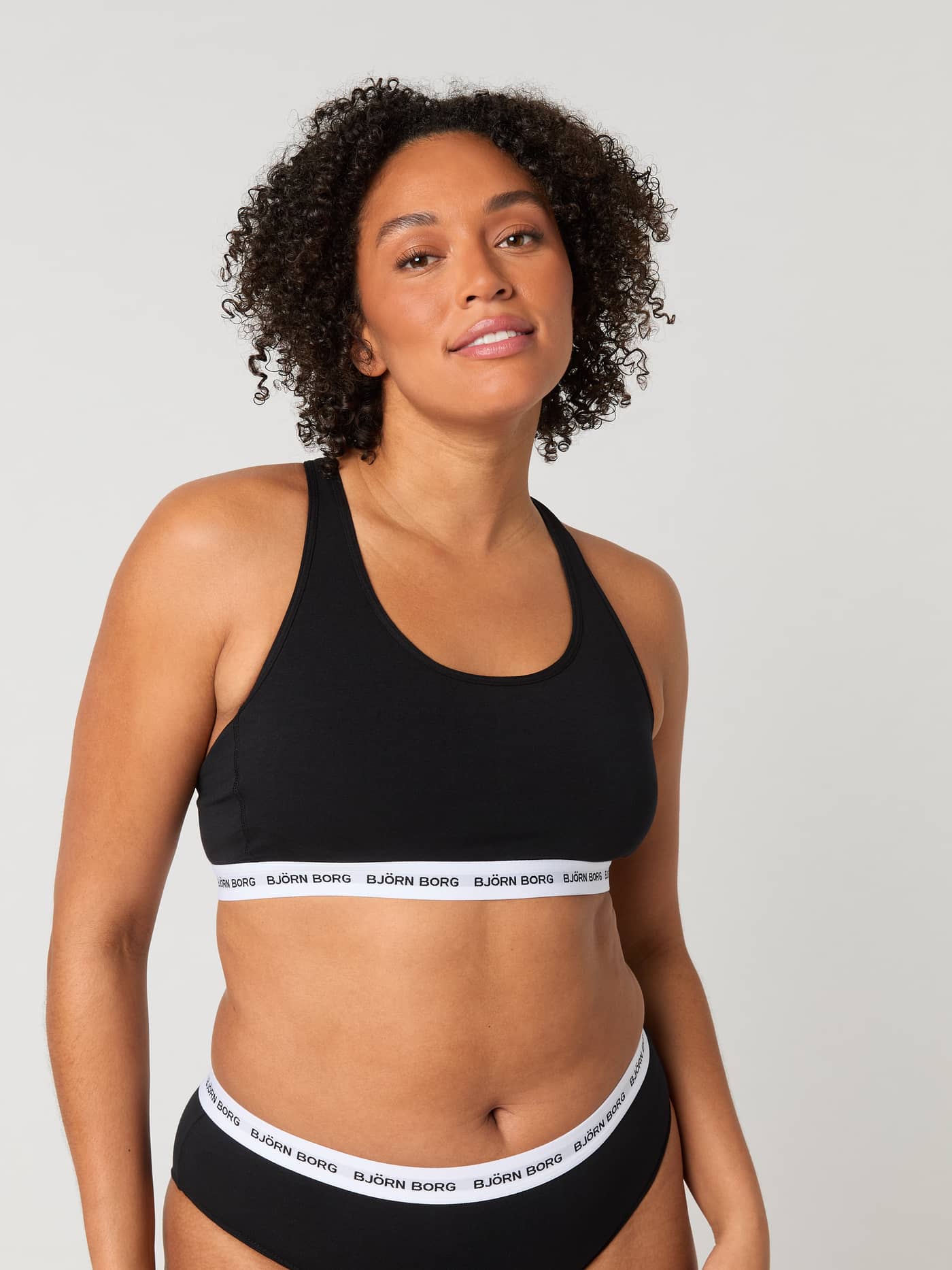 Vista frontal de una modelo con el Core Logo Soft Top 1-pack en Negro, elástico de logo blanco y diseño de espalda nadadora. - Image 3