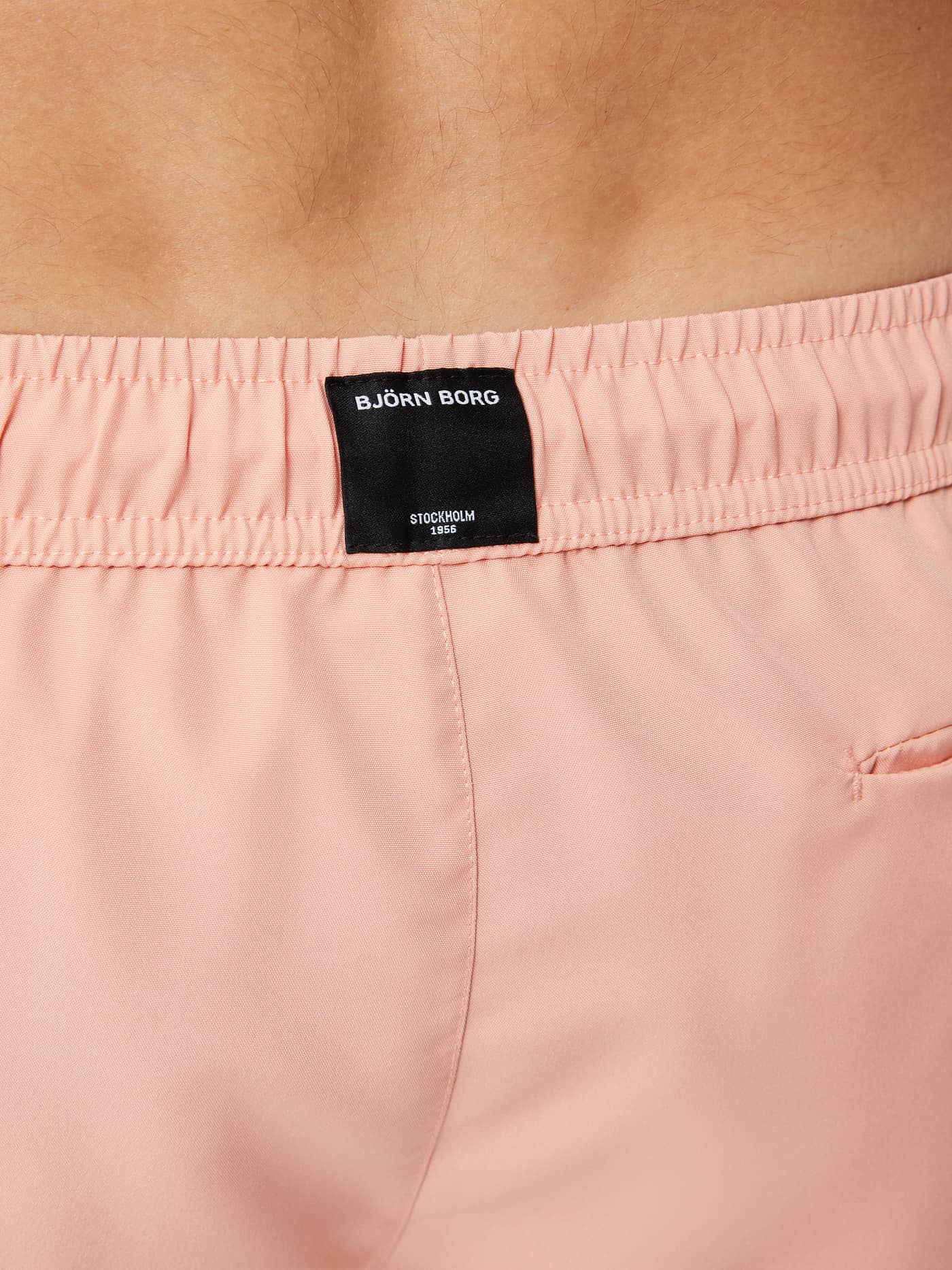 Detailansicht der Rückseite der Borg Retro Swim Shorts in Coral Almond (Rosa) mit schwarzem gewebten Logo-Label. - Image 5