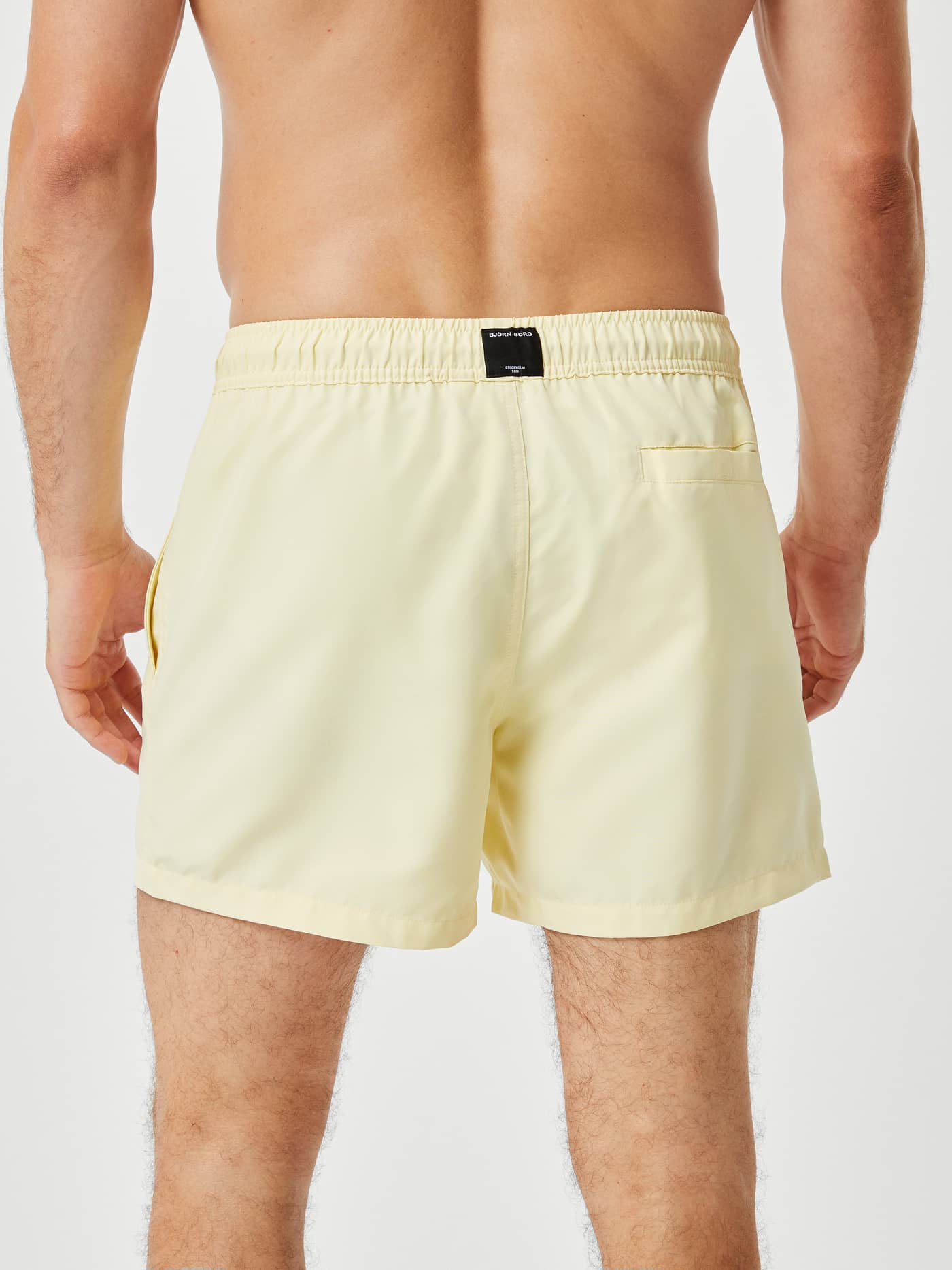Vue arrière d'un homme en Borg Solid Swim Shorts French Vanilla (Jaune) avec logo noir et poche à Velcro. - Image 3