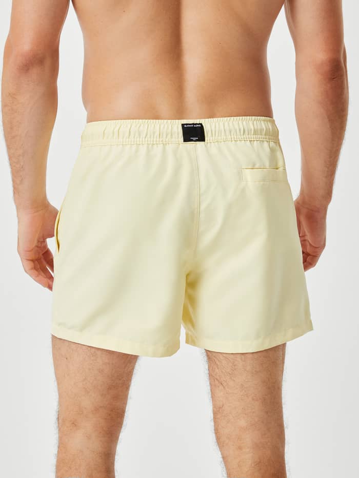 Borg Solid Swim Shorts in French Vanilla (Geel) in achteraanzicht met een zwart logolabel en achterzak met klittenband. - Image 3