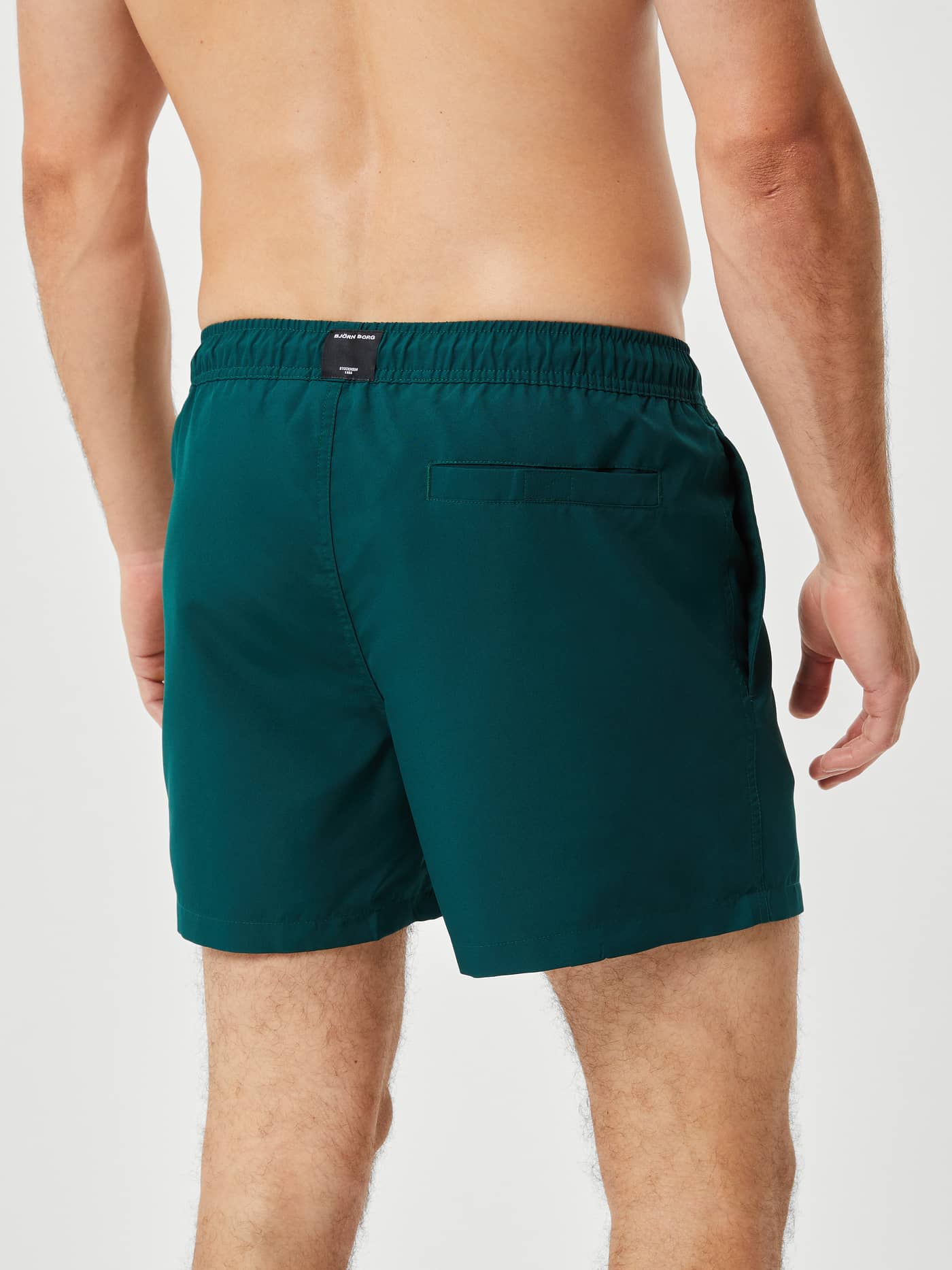 Back view of a man wearing loose-fit Borg Solid Swim Shorts in Ponderosa Pine (Green) with a functional back pocket. - Image 3
