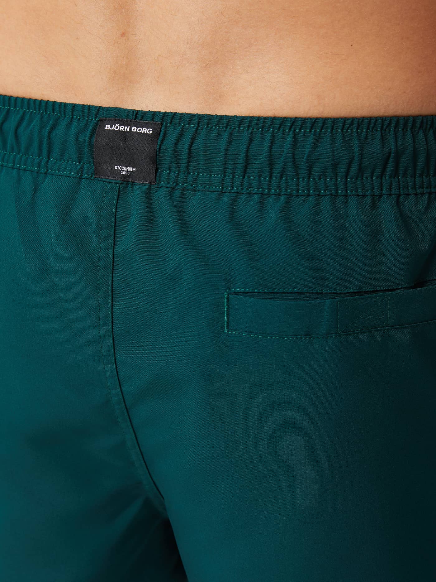 Detailed close-up of the Borg Solid Swim Shorts in Ponderosa Pine (Green) showing the black logo label and back pocket. - Image 4