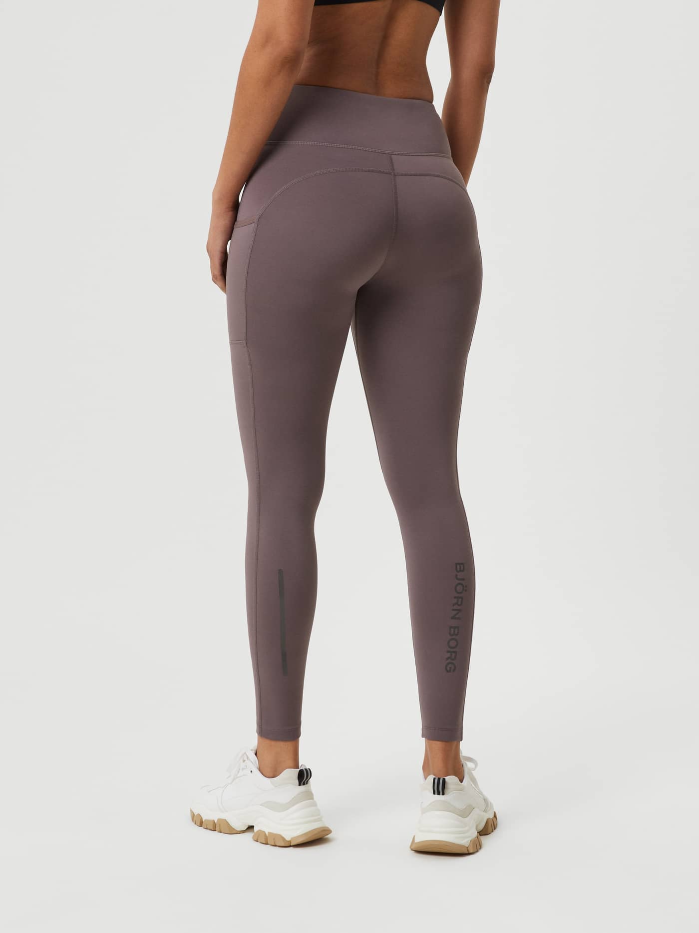 Back view of a model in Sparrow (Brown) Borg Running Tights, with a black logo and reflective strips for a performance fit. - Image 1
