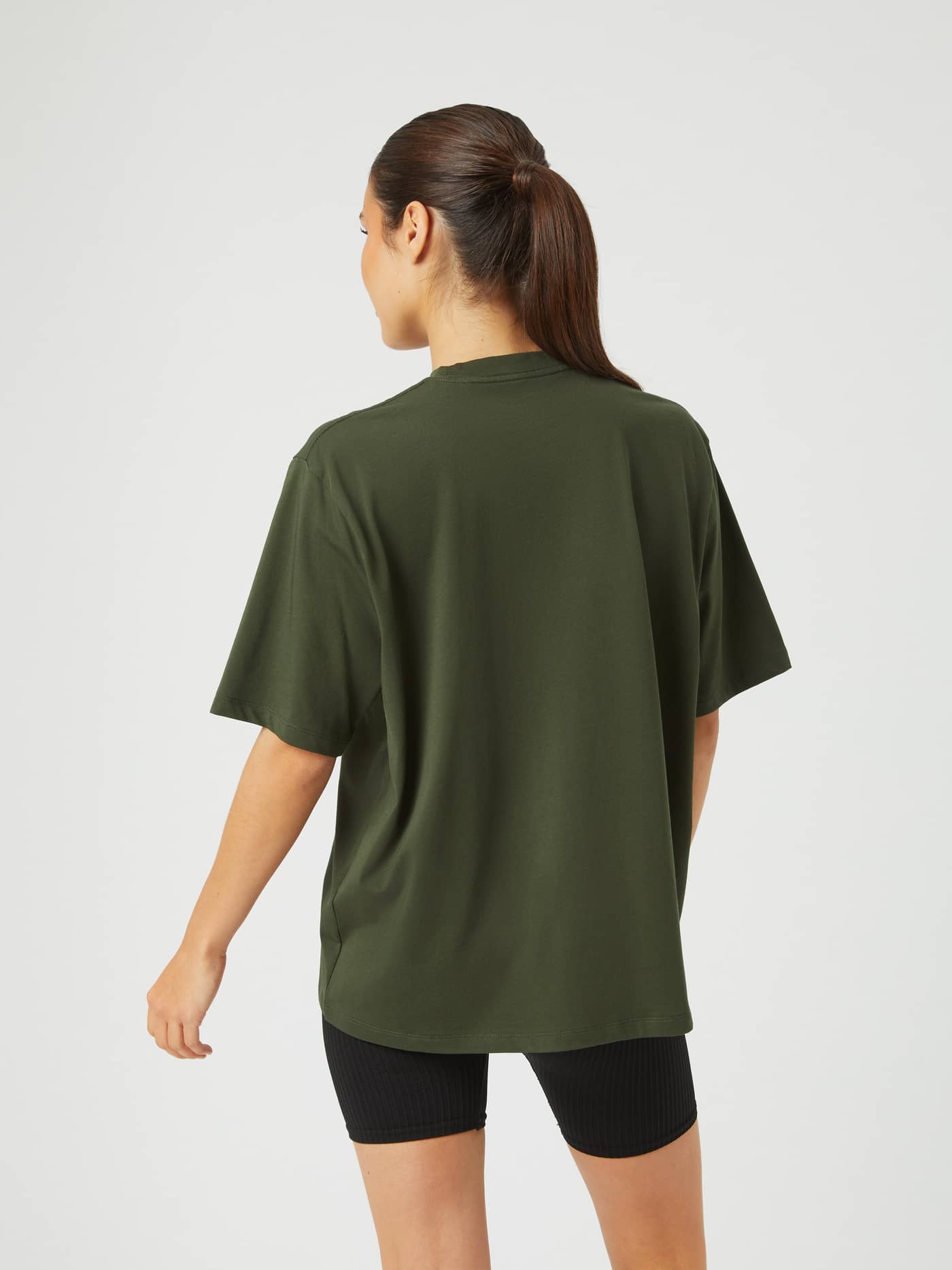 Back view of a model wearing the loose fit Studio Oversized T-Shirt in Duffel Bag (Green) for training. - Image 2
