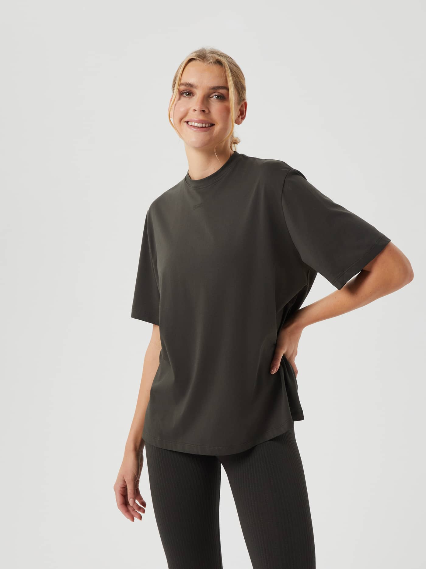 Front view of a woman wearing the Björn Borg Studio Oversized T-Shirt in Peat (Green), a loose fit for training style. - Image 1