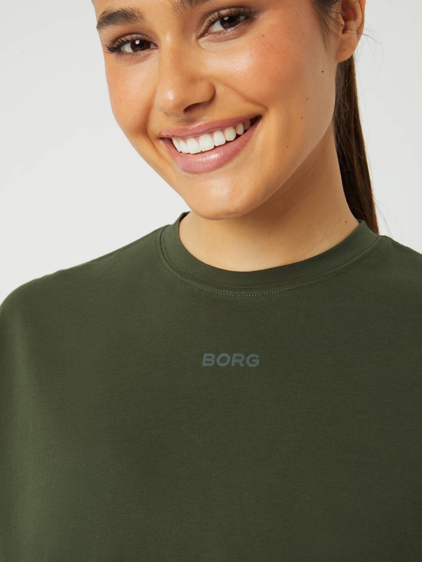 Björn Borg Studio Oversized T-Shirt in Duffel Bag (Green) worn by a smiling woman, close-up with a grey logo for training. - Image 4