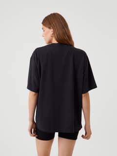 Back view of a woman wearing the Studio Oversized T-Shirt in Black Beauty (Black), featuring a loose and relaxed fit. - Image 5