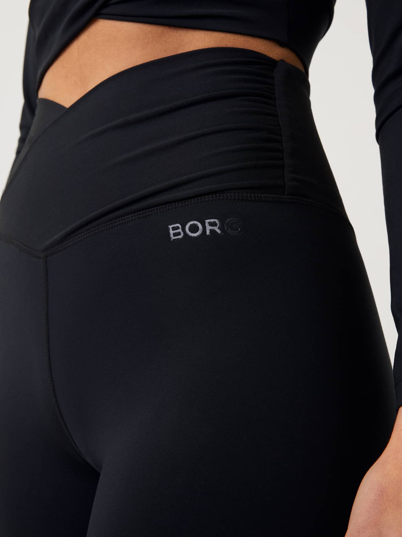 Close-up of the Studio Cross Shorts in Black Beauty (Black), showcasing the overlap waistband and grey BORG hip logo. - Image 4