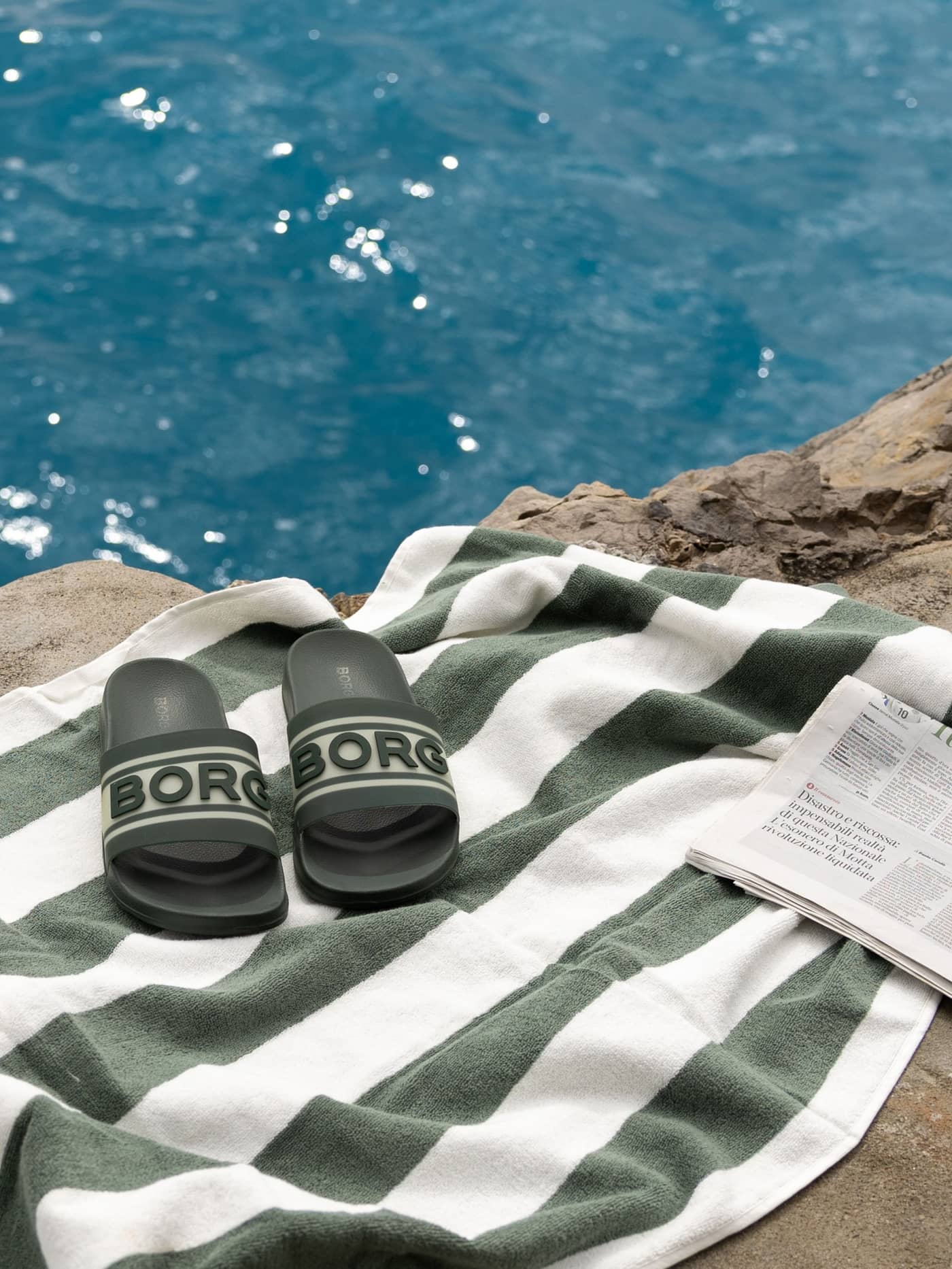 Green Men’s Sandal Knox pool slides in TPU rubber with a dark green logo, resting on a striped towel by the sea. - Image 4