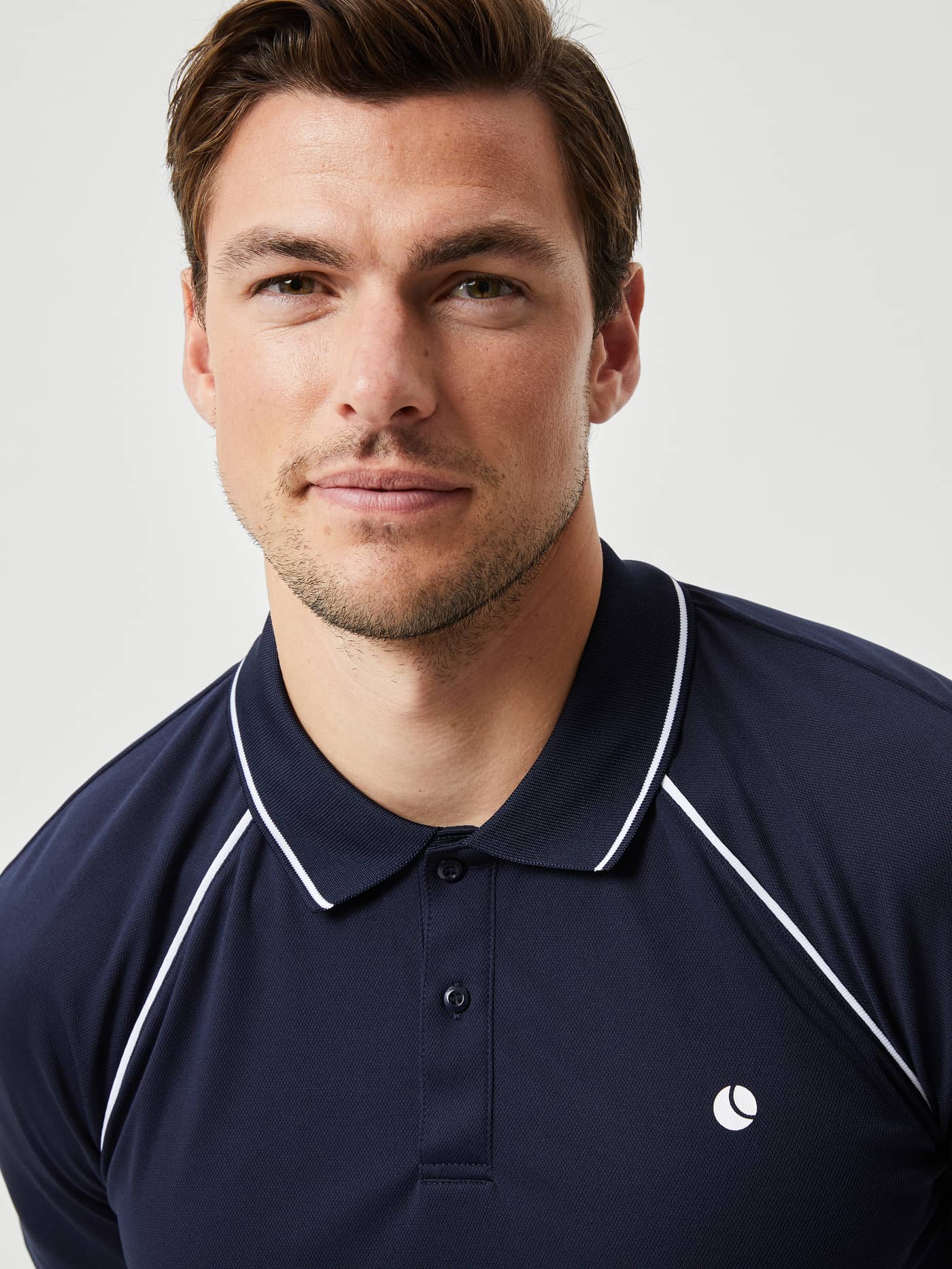 Close-up of a man wearing the Björn Borg Ace Racquet Polo in Night sky (Blue), a tennis shirt with white piping and logo. - Image 4