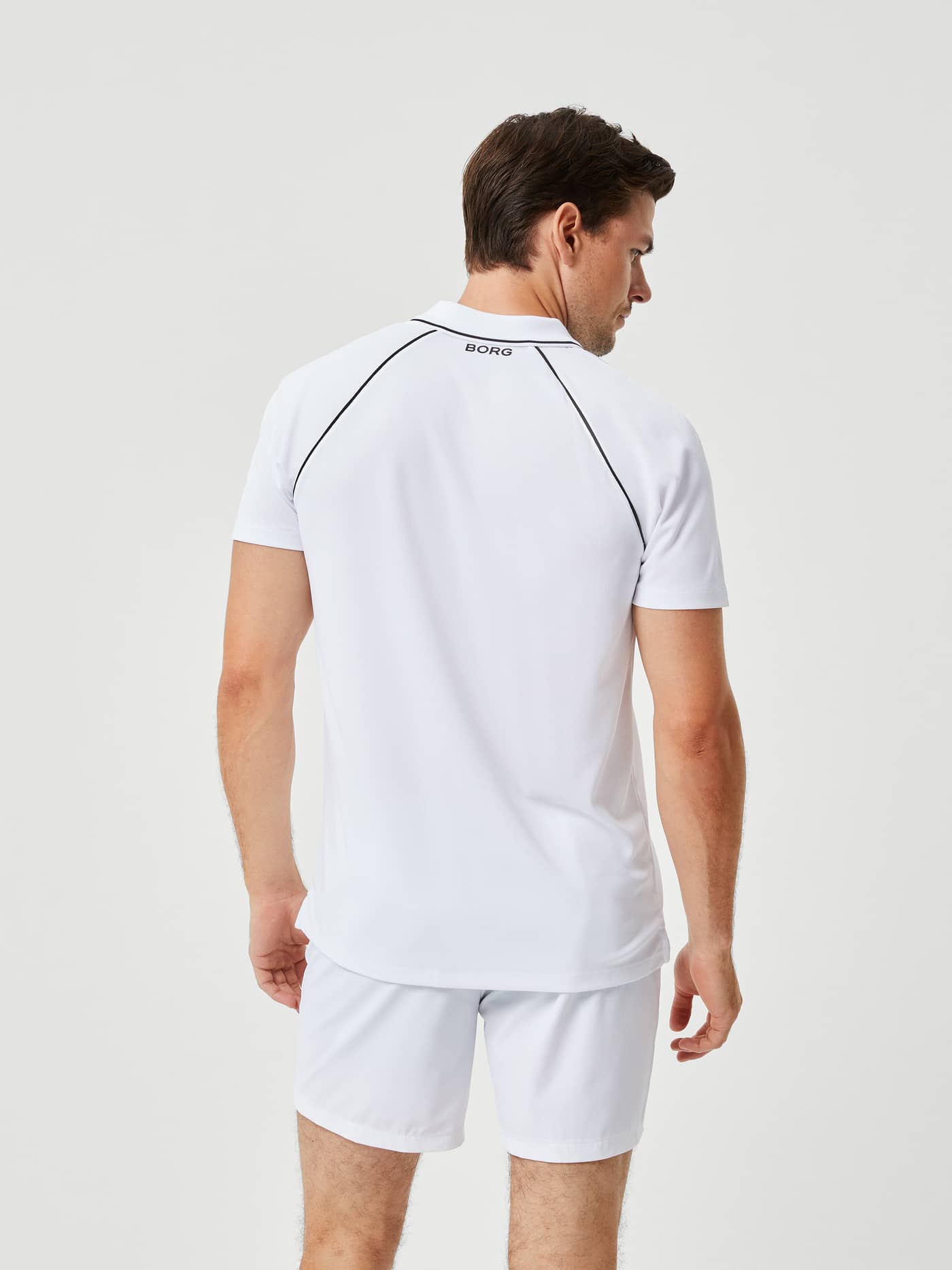 Back view of a man in the Ace Racquet Polo in Brilliant White (White), a performance tennis shirt with black logo and piping. - Image 2