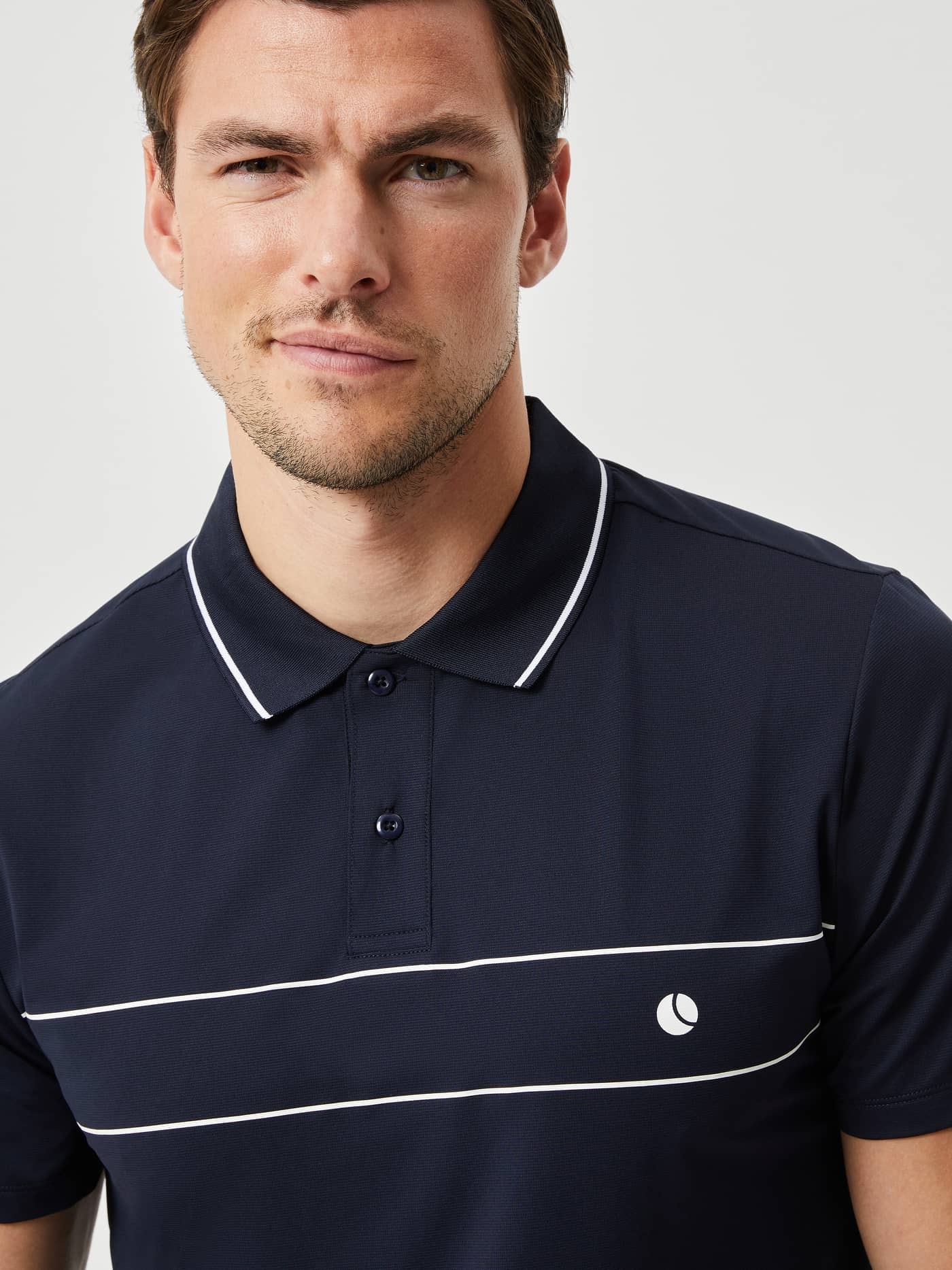 Ace Light Polo i Night Sky (Blå) set i nærbillede med tennisboldlogo, en funktionel og stilfuld polo til tennis. - Image 4