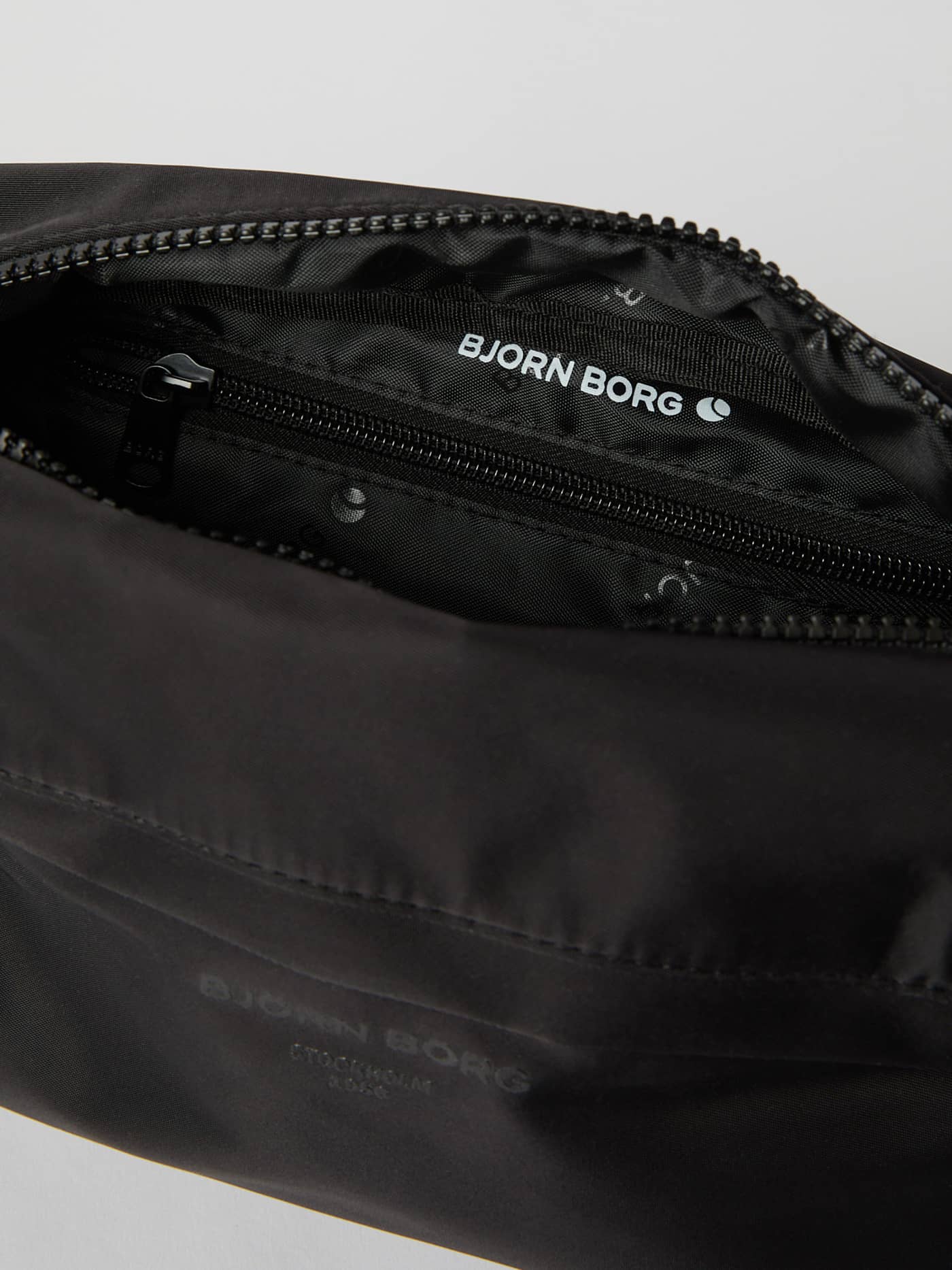 Detailed interior view of the Borg Daily Crossover Bag in Black Beauty (Black) featuring a zippered pocket and white logo. - Image 4