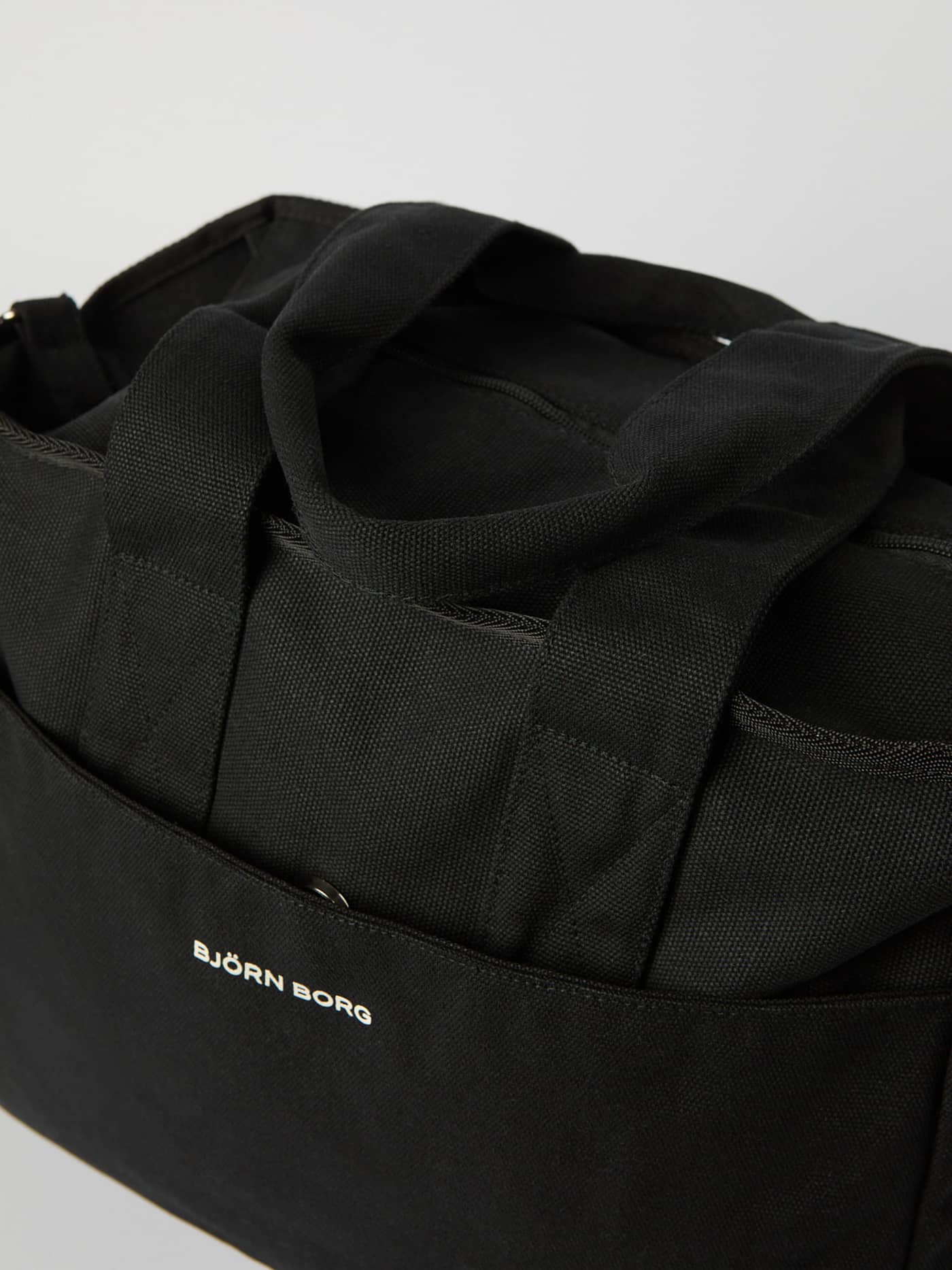 Close-up of the Studio Canvas Tote 27L in Black Beauty (Black) featuring durable cotton canvas and a stylish white logo. - Image 3