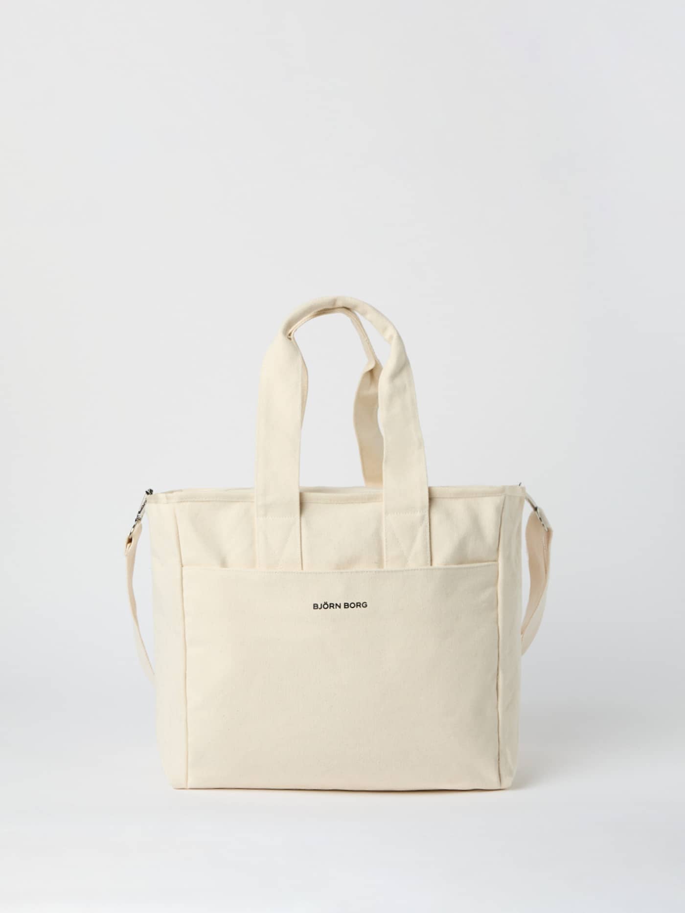 Front view of the Studio Canvas Tote 27L in Egret (White), featuring durable cotton canvas and a black logo. - Image 1