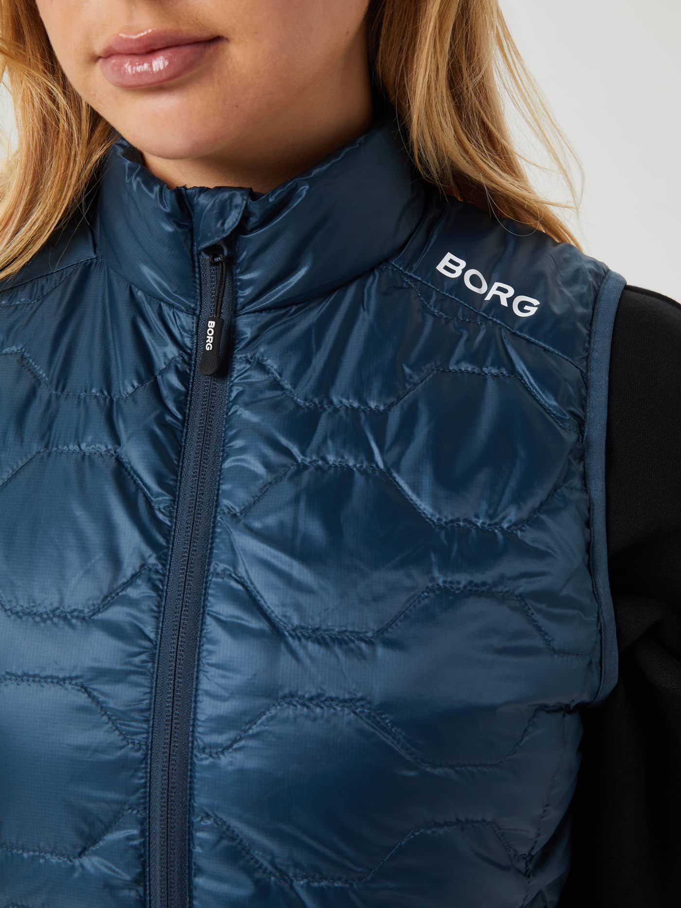Gros-plan d'une femme portant le Borg Down Liner Vest matelassé en Midnight Navy (Bleu marine) avec logo blanc. - Image 4