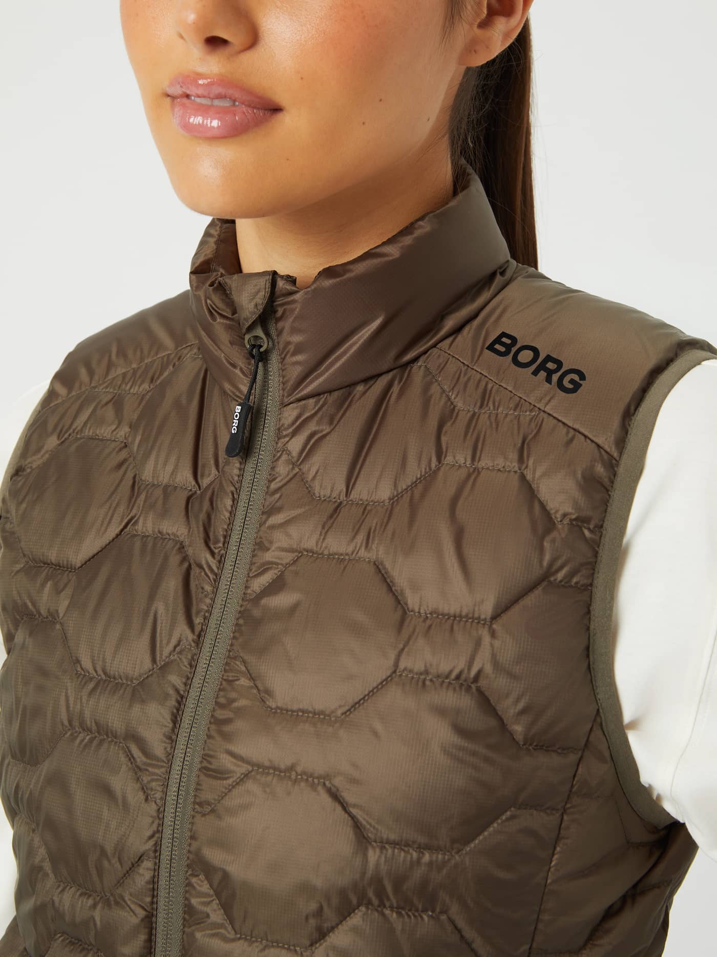 Borg Down Liner Vest in Tarmac (Brown) with a quilted hexagonal pattern and black logo in a close-up. - Image 5
