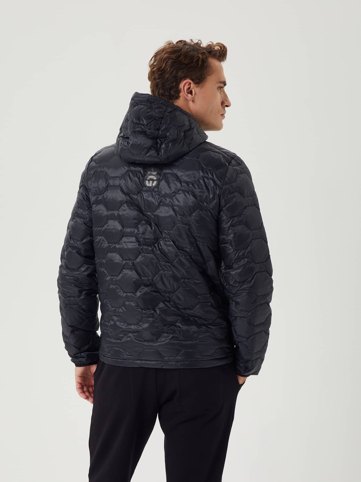 Back view of a man wearing the quilted Borg Down Liner Jacket in Black Beauty (Black) featuring a silver back logo. - Image 4
