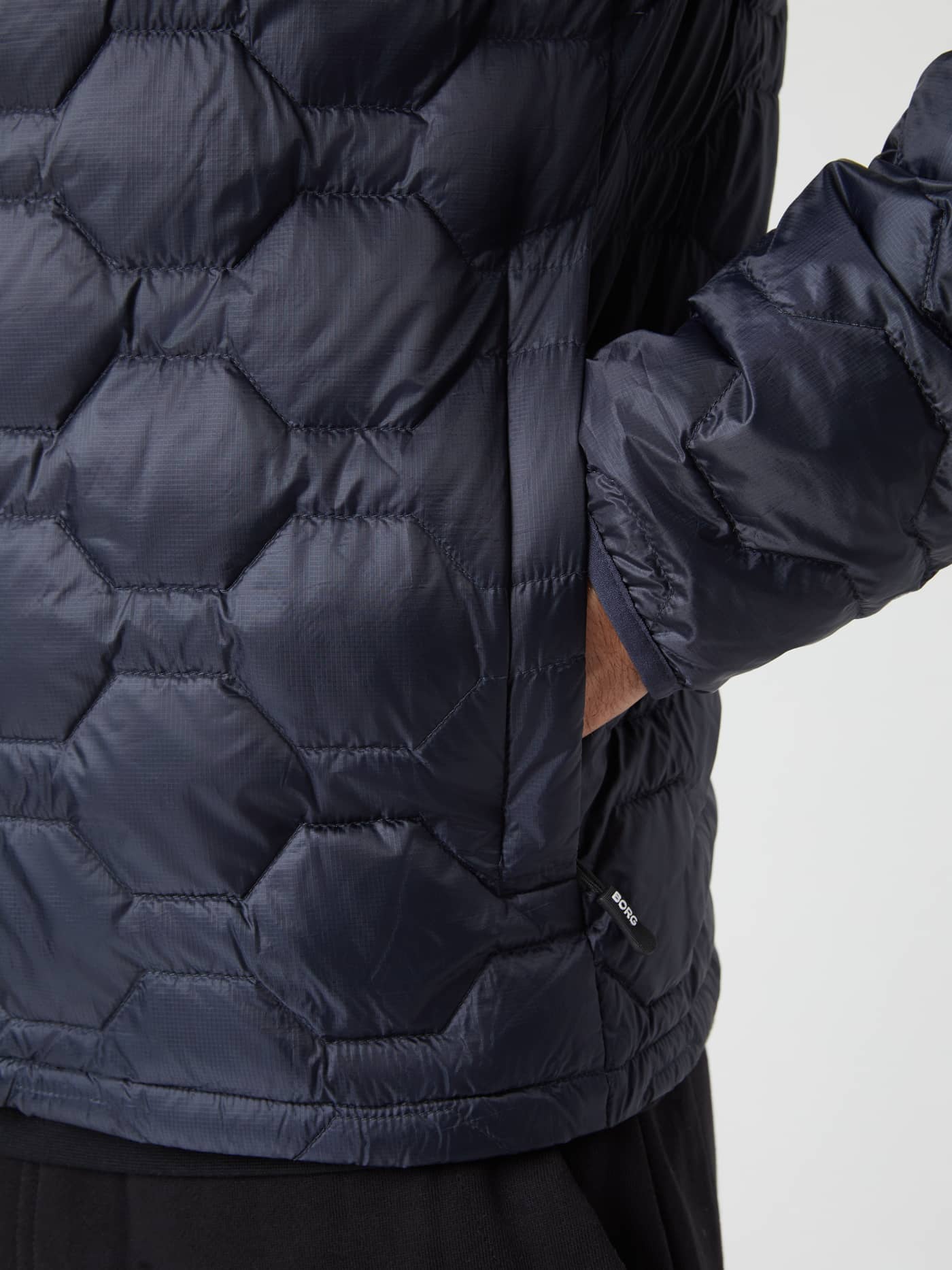Närbild på hexagonquiltade Borg Down Liner Jacket i Night sky (Marinblå) för herr med ficka och vit logotyp. - Image 6