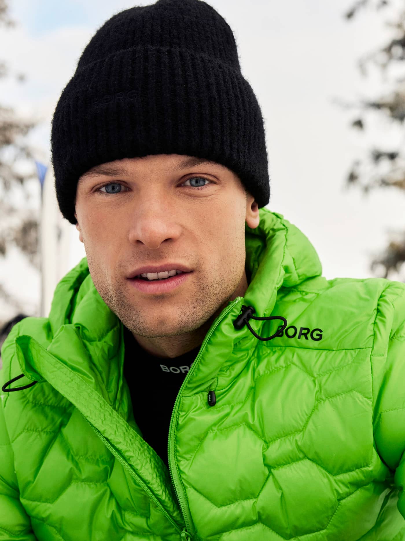 Front view of a man wearing the green Björn Borg Down Liner Jacket with a black logo and adjustable drawstring hood. - Image 1