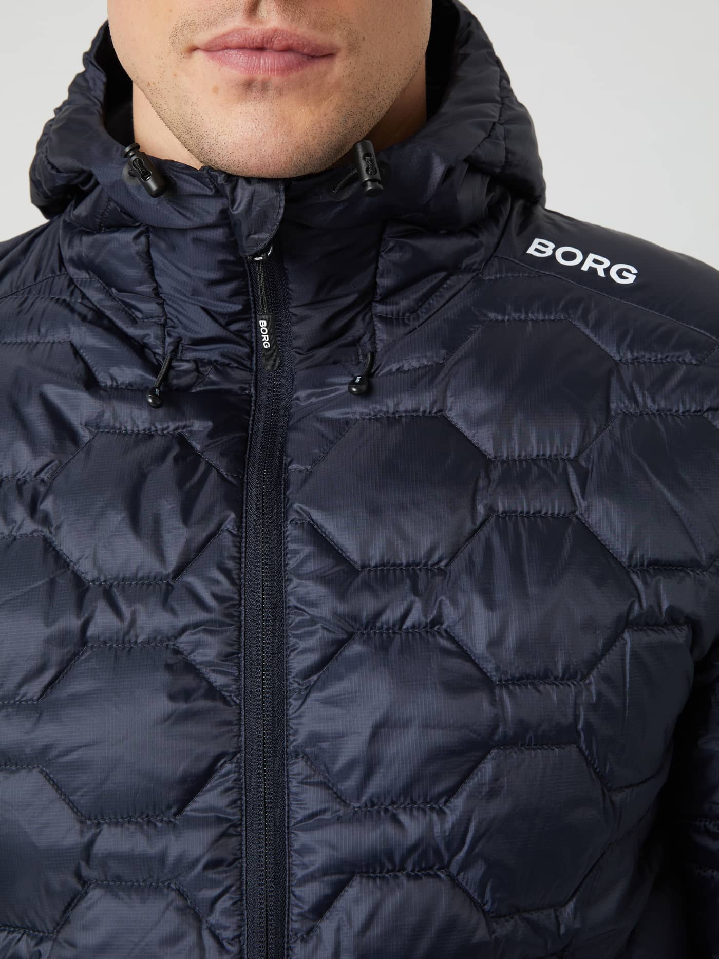 Närbild framifrån på Borg Down Liner Jacket i Night Sky (Blå) för herrar med vit BORG-logotyp och sexkantig kviltning. - Image 4