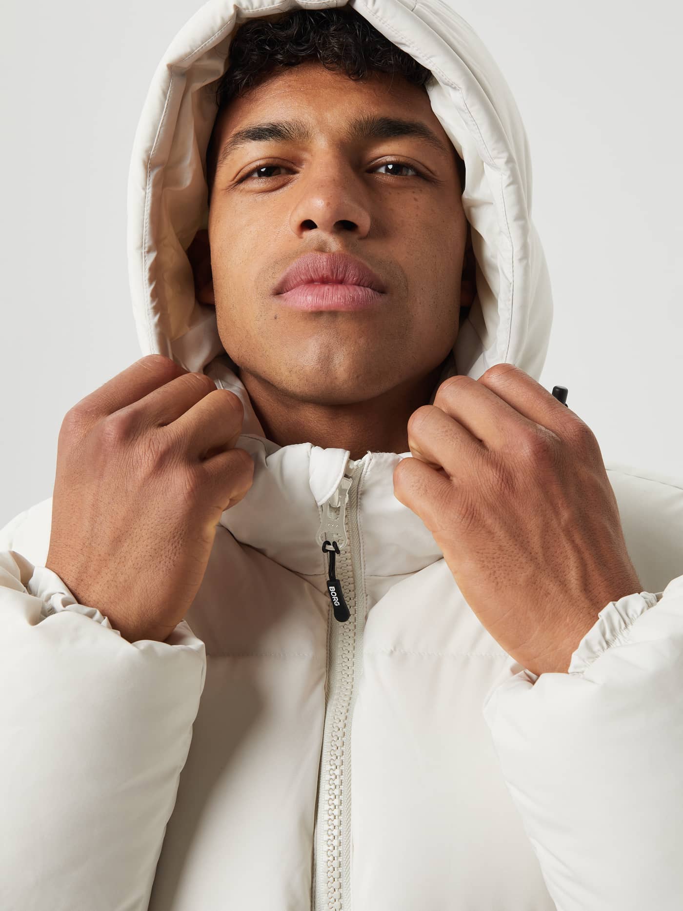 Close-up of a man wearing the Björn Borg Centre Puffer Jacket in Silver Birch (White) with the hood up. - Image 4