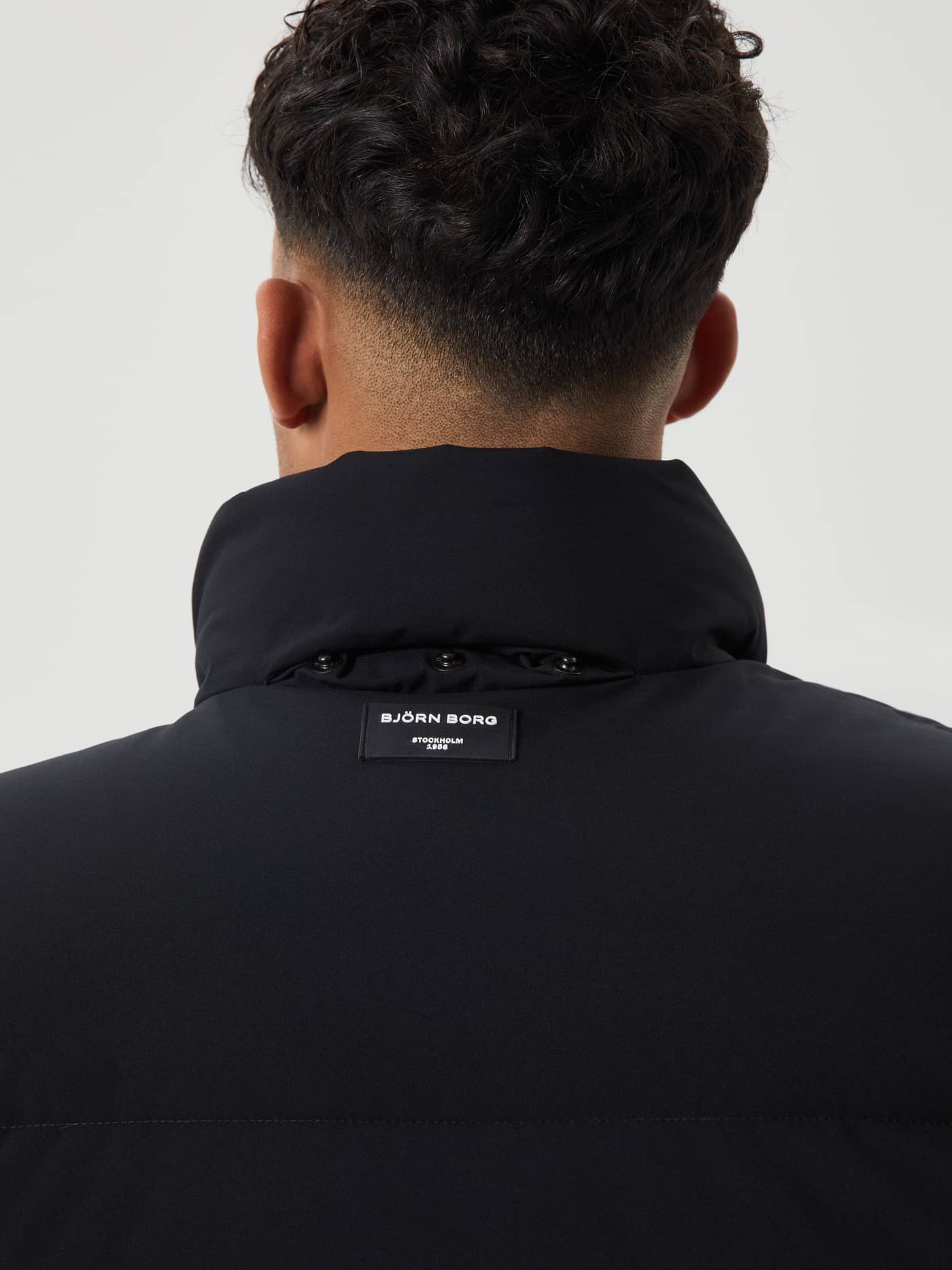 Back view of a man wearing the functional Centre Puffer Jacket in Black Beauty (Black) featuring a white Björn Borg logo. - Image 7