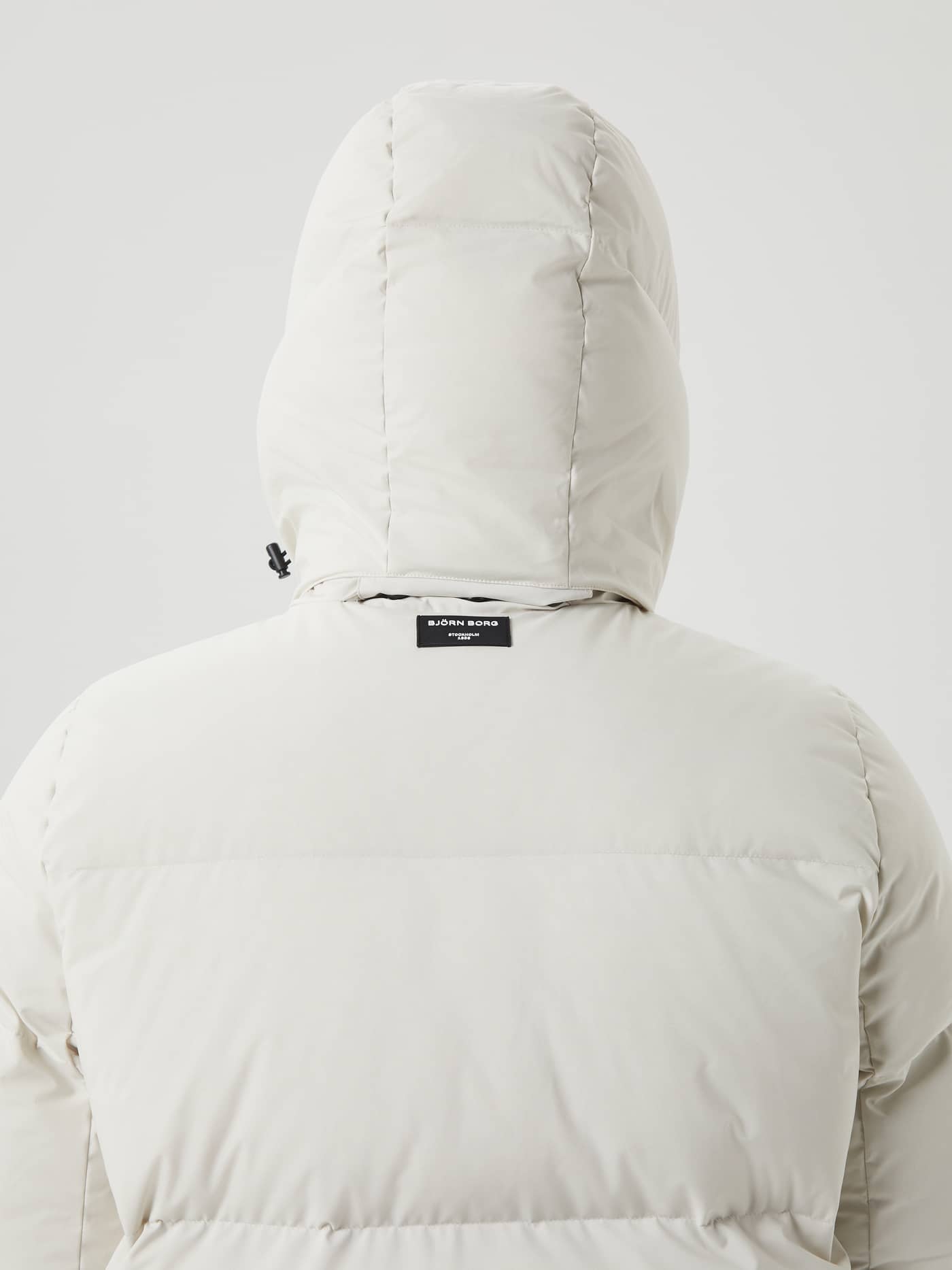 Back view of a man wearing the Björn Borg Centre Puffer Jacket in Silver Birch (White) with a hood and black logo. - Image 7
