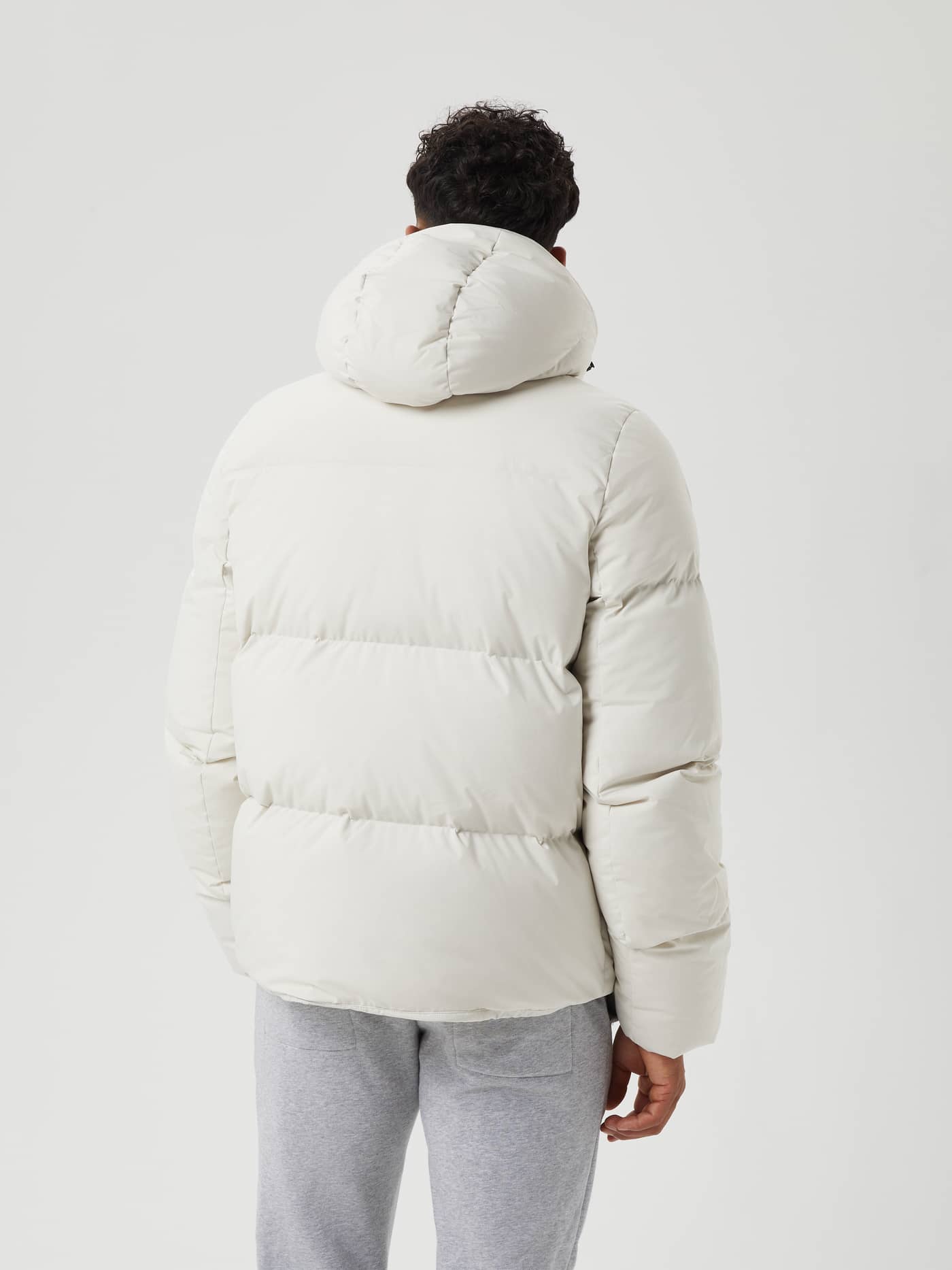 Back view of a man wearing the Björn Borg Centre Puffer Jacket in Silver Birch (White), featuring a functional hood. - Image 3
