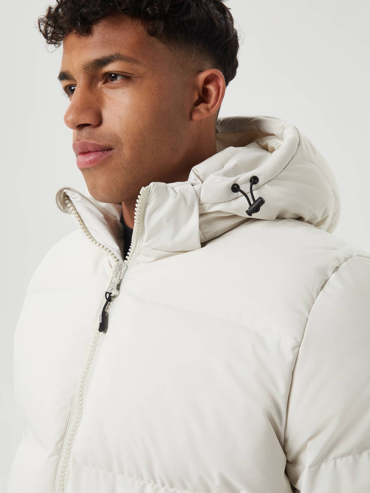 Close-up profile of a man wearing the down-filled Björn Borg Centre Puffer Jacket in Silver Birch (White) with a black logo. - Image 6