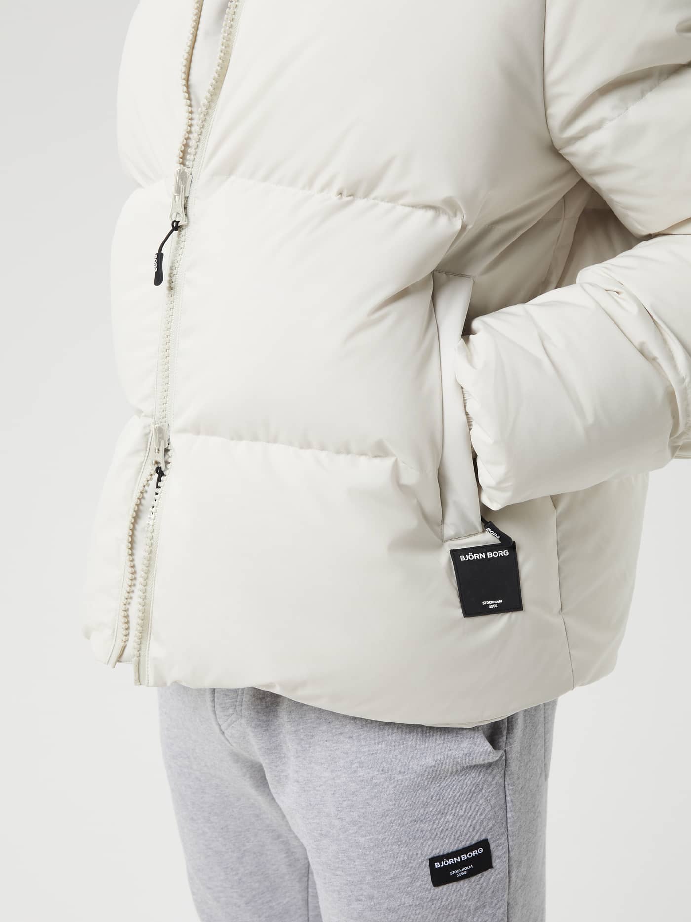 Detailed close-up of the Centre Puffer Jacket in Silver Birch (White) for men, featuring a black logo tag on the pocket. - Image 5