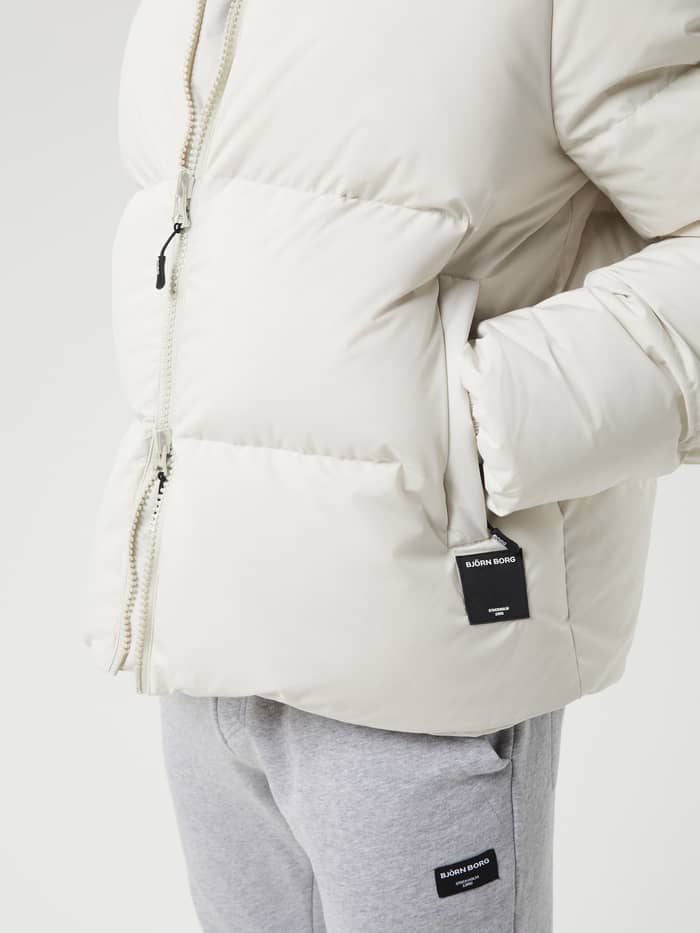 Detailed close-up of the Centre Puffer Jacket in Silver Birch (White) for men, featuring a black logo tag on the pocket. - Image 5