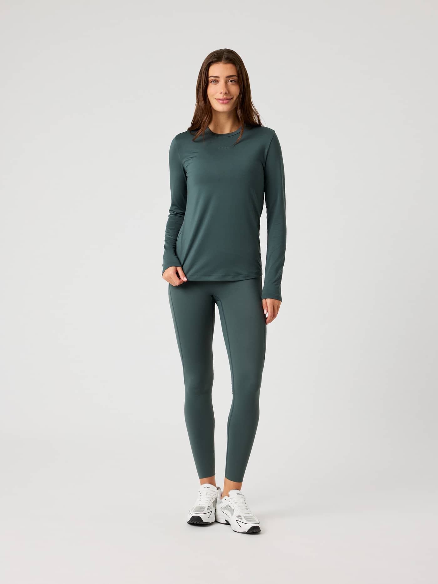 Full-body front view of a woman in the Borg Long Sleeve T-Shirt in Urban Chic (Green) and matching training leggings. - Image 3