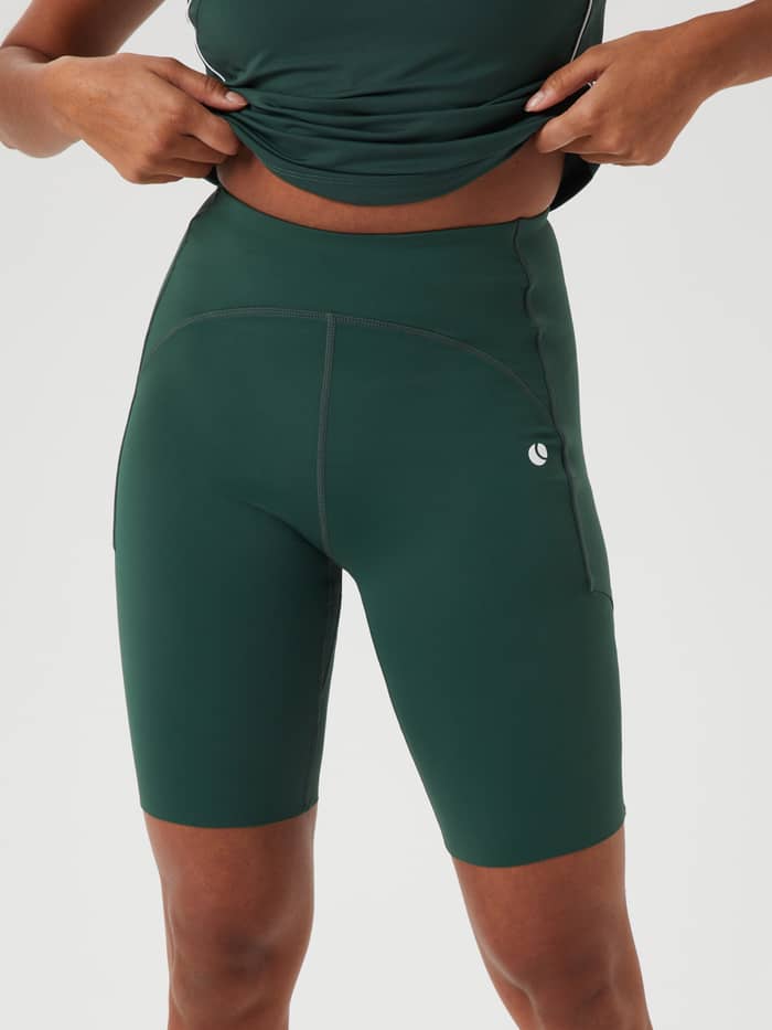 De Ace Biker Shorts in Sycamore (Groen) voor tennis met een hoge taille, slanke pasvorm en een wit tennisballogo.