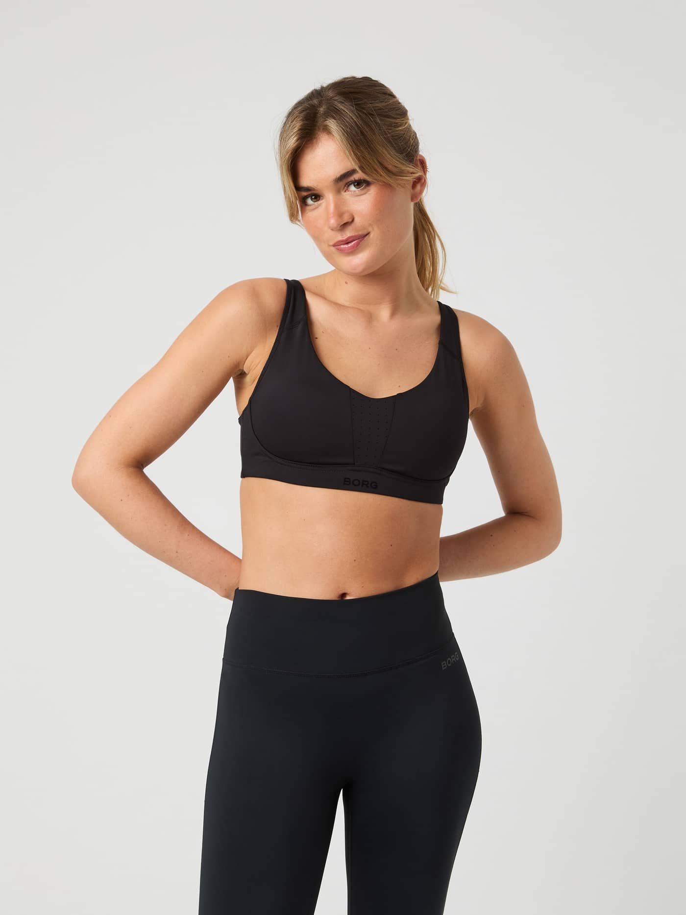 Front view of a model wearing the black Borg Reform Sports Bra with her hands behind her back. - Image 7