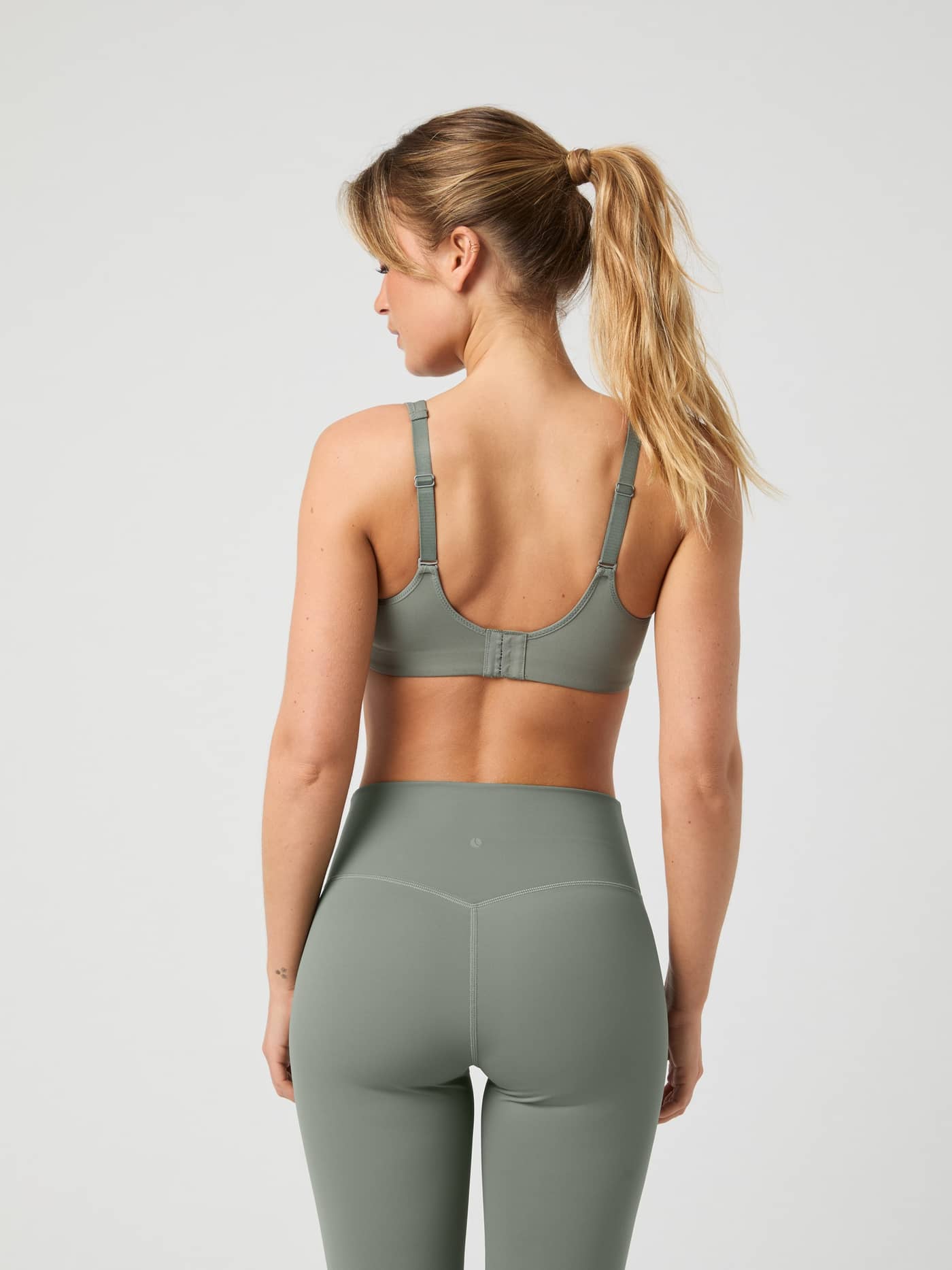 Back view of a model in the Agave Green Borg Reform Sports Bra, showing the adjustable straps and hook-and-eye clasp. - Image 11