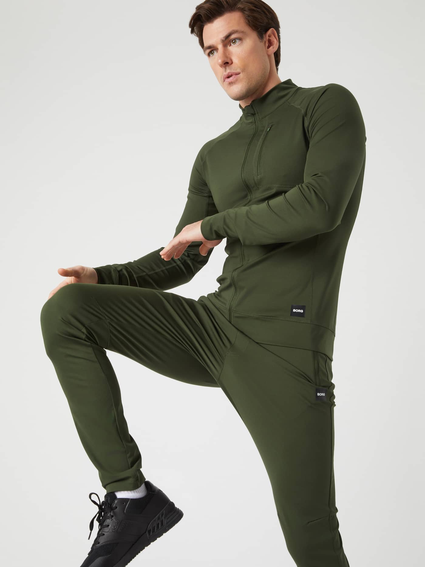 Action view of a man wearing the Borg Training Midlayer Jacket in Duffel Bag (Green) for a functional training look. - Image 5