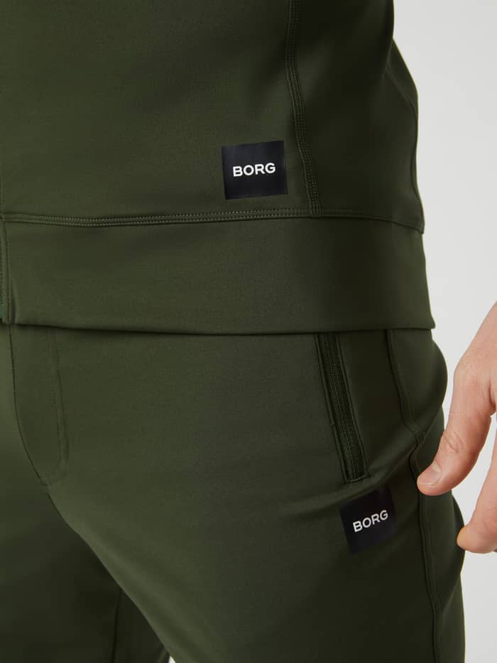 Close-up of the Duffel Bag (Green) Borg Training Midlayer Jacket for men, showcasing the logo and functional style. - Image 4