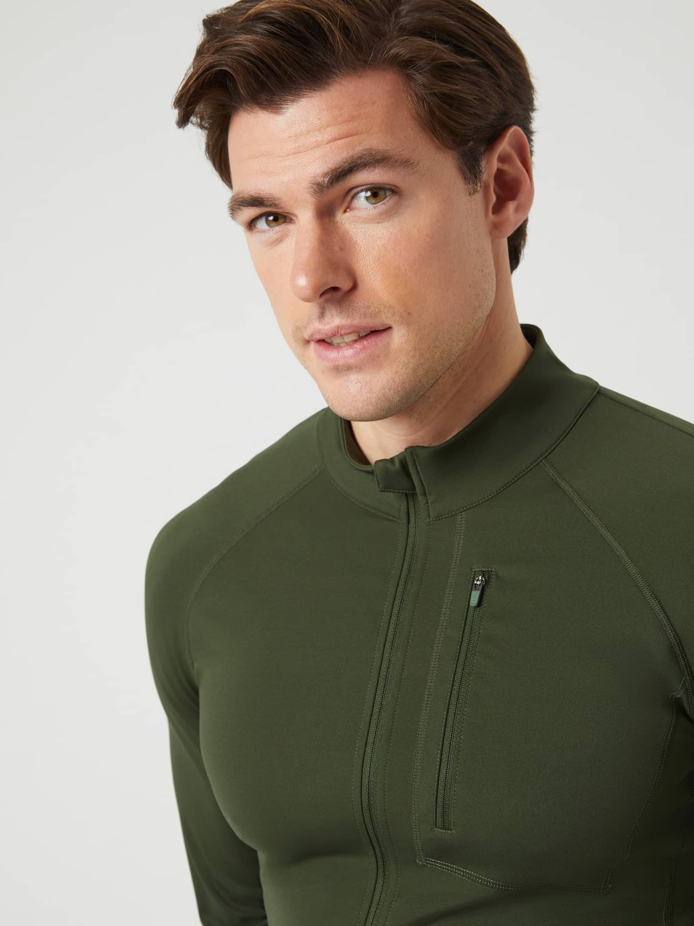 Close-up of a man wearing the Borg Training Midlayer Jacket in Duffel Bag (Green) with a zippered chest pocket. - Image 6