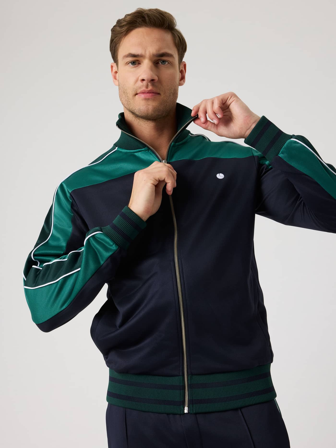 Front view of a man zipping the Björn Borg Ace Retro Track Jacket in Night sky (Navy) for a classic, functional tennis look. - Image 4