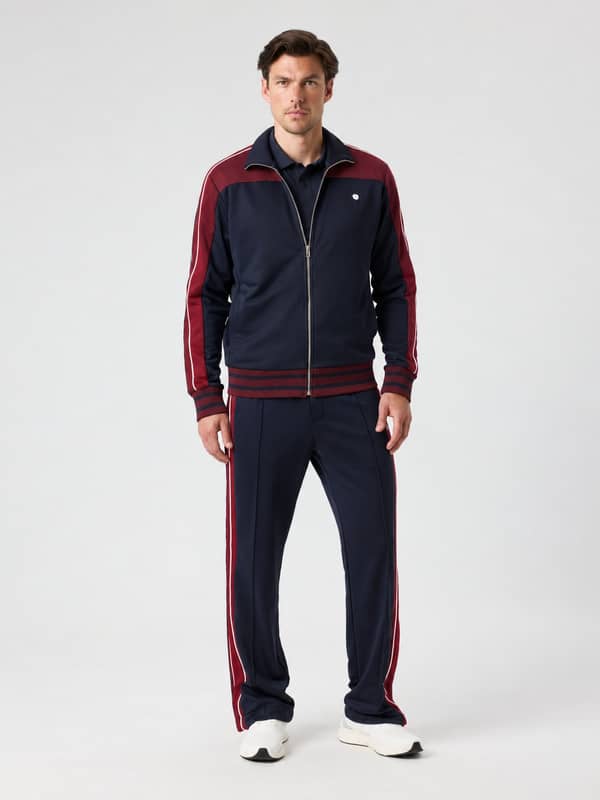 Vooraanzicht van de Ace Retro Track Pants in Night sky (Marine) met contrasterende kleurpanelen en tennisballogo.