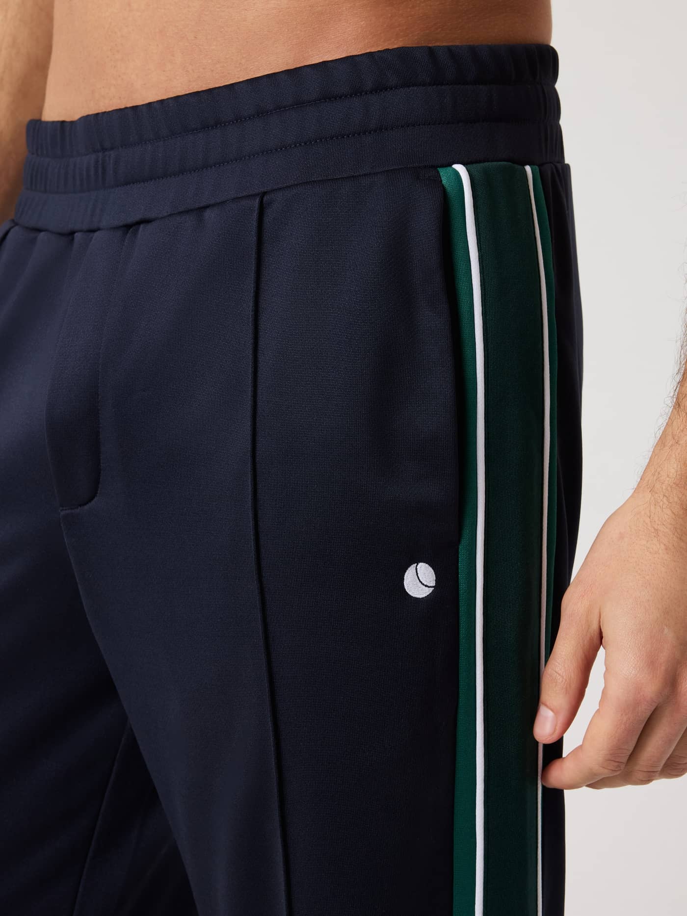 Nærbillede af Ace Retro Track Pants i Night Sky (Navy) med grøn sidestribe og hvidt tennisboldlogo til tennis. - Image 5