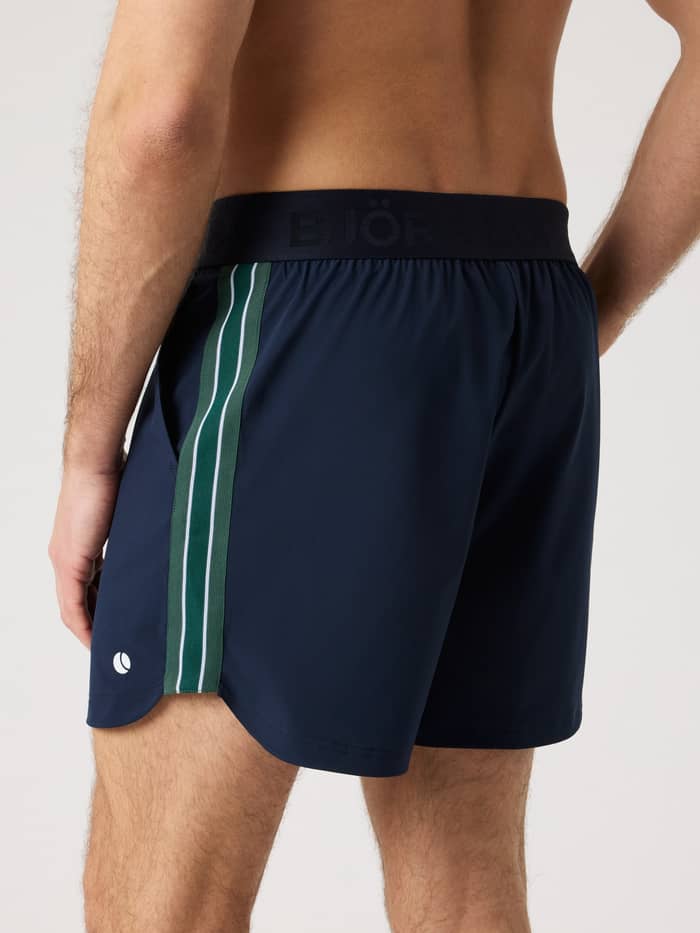 Ace Retro Shorts 6 Inch i Night Sky (Marineblå) set fra siden med retrostriber og et hvidt tennisboldlogo til tennis. - Image 2