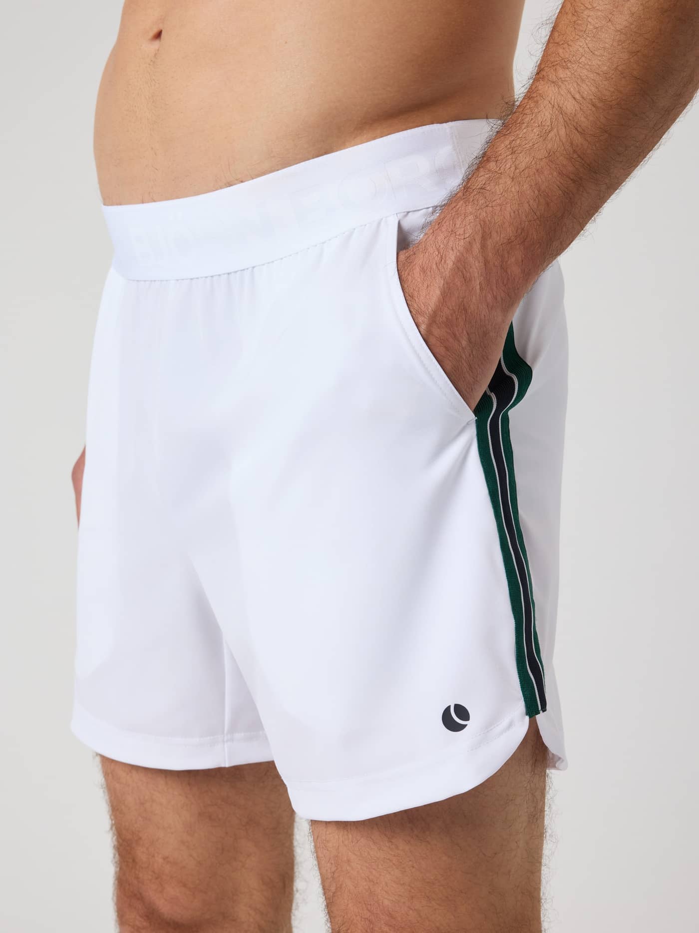 Side view of a man in the tennis Ace Retro Shorts 6 Inch in Brilliant White (White) with a black logo and side stripes. - Image 3
