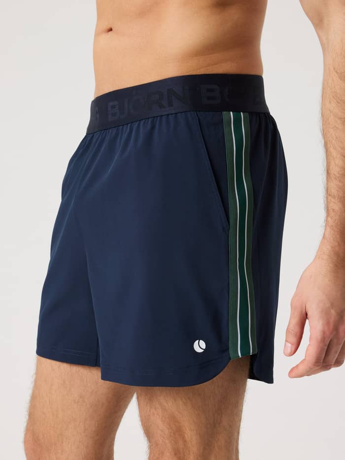 Ace Retro Shorts 6 Inch in Night sky (Marineblauw) met retrostrepen en een wit tennisballogo, getoond in zijaanzicht.