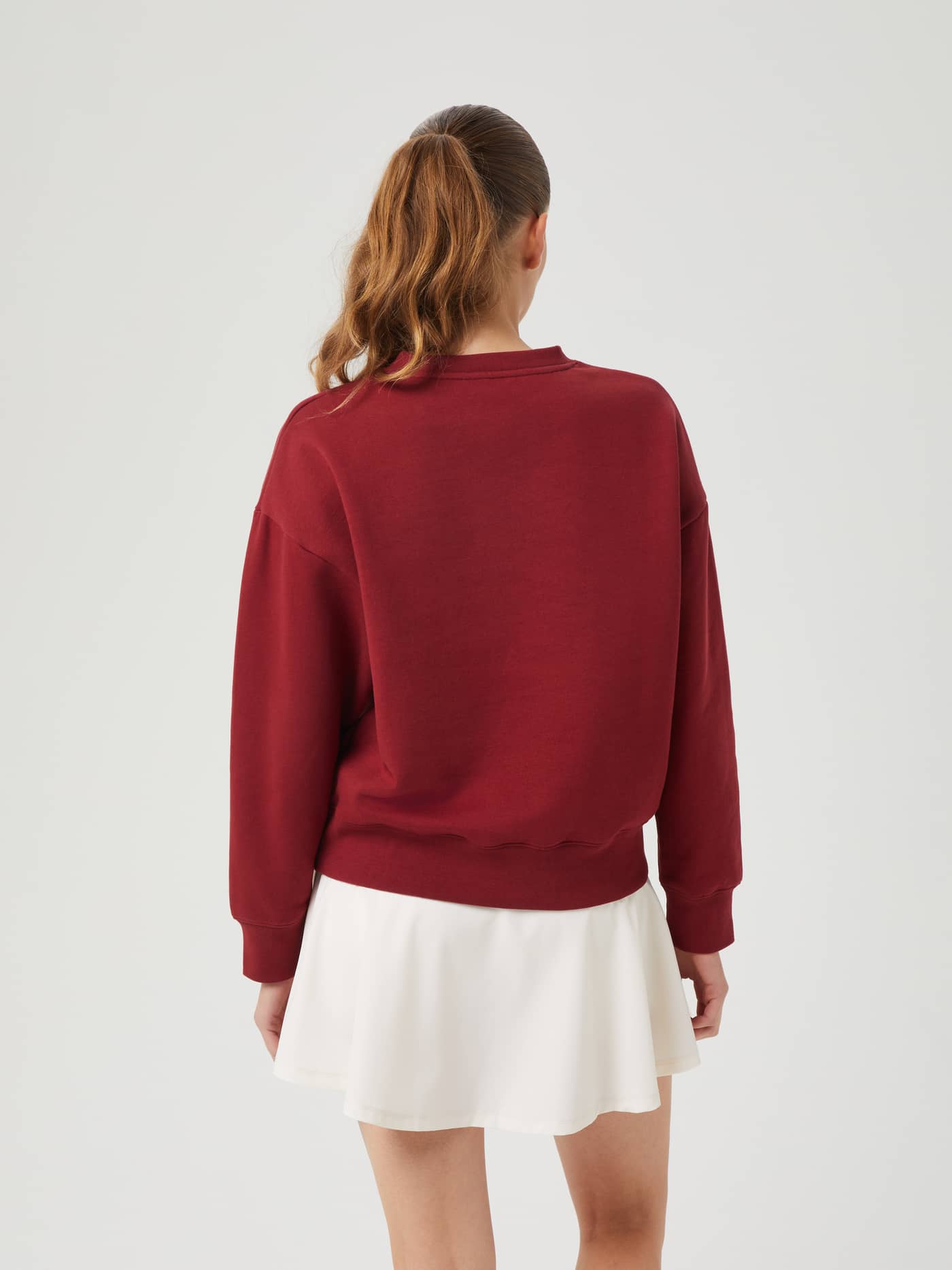 Back view of a model wearing the oversized Borg Boyfriend Crew in Pomegranate (Red) paired with a white skirt. - Image 3